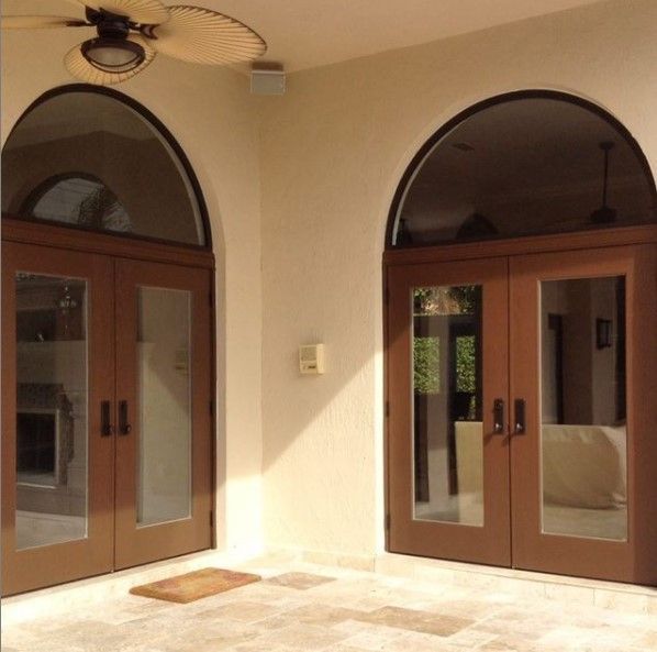 Two arched brown double doors with glass panels on a patio.