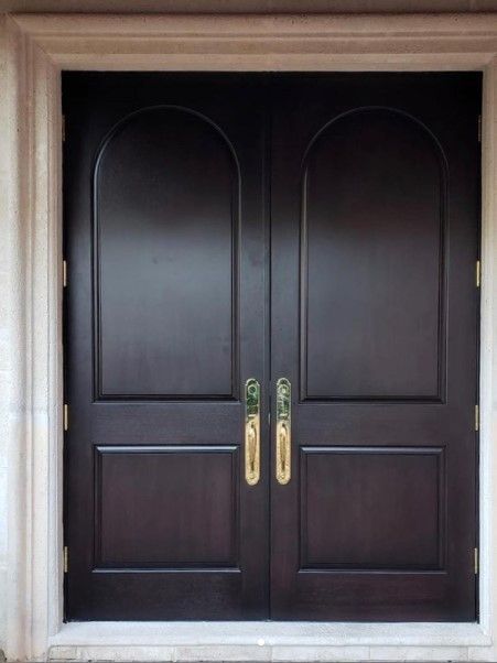 Dark wooden double doors with arched top and gold handles.