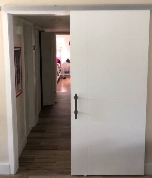 White sliding door open, revealing a hallway with hardwood floors and a room in the distance.