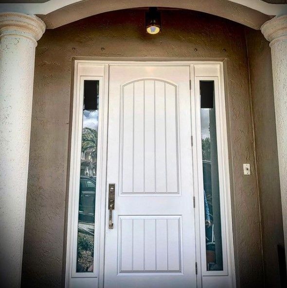 White front door with sidelights, under an arched entryway, between white pillars.