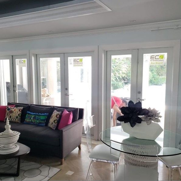 Living room with a gray sofa, glass table, and french doors overlooking a yard.