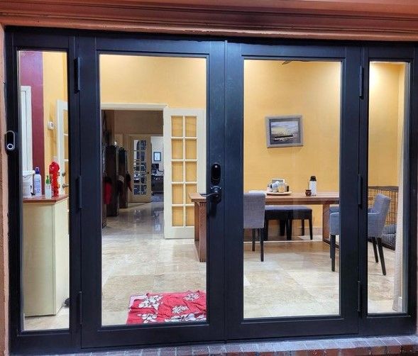 Black-framed glass doors open to a dining area with a table and chairs, and views into other rooms.