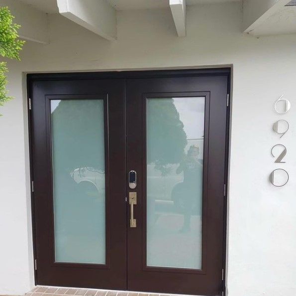 Brown double doors with frosted glass panels, a black lock, and the house number 0920 on a white wall.