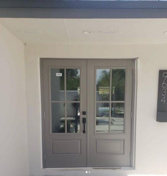 Grey double doors with glass panes, set in a white wall. A black address sign is visible.