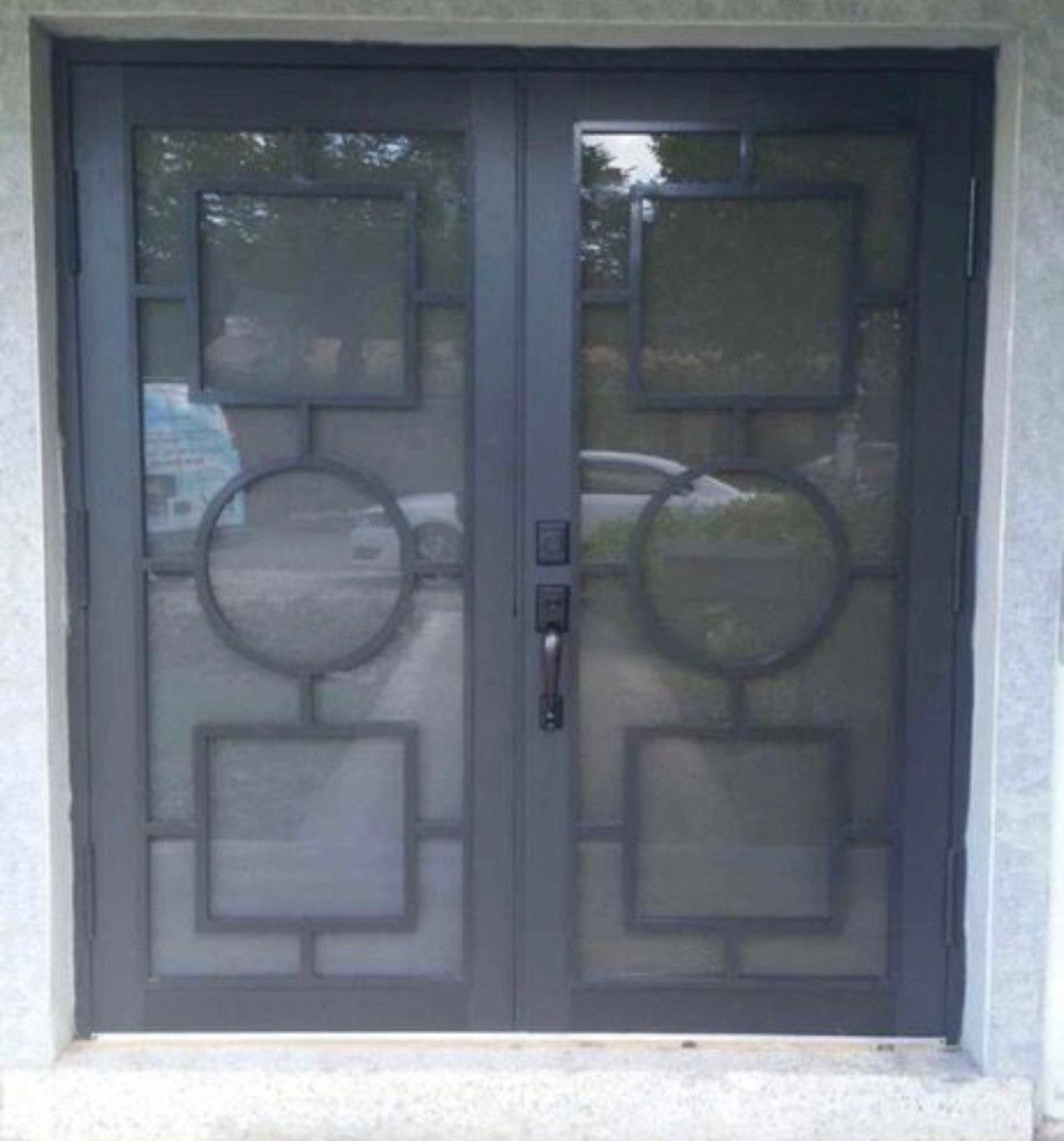 Dark gray double doors with geometric ironwork and glass panels.