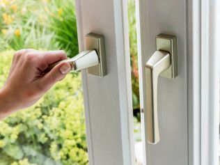 Hand turning a white window handle, opening a window with a green outdoor view.
