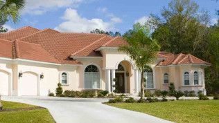 Light peach stucco home with clay tile roof and a long driveway on a sunny day.
