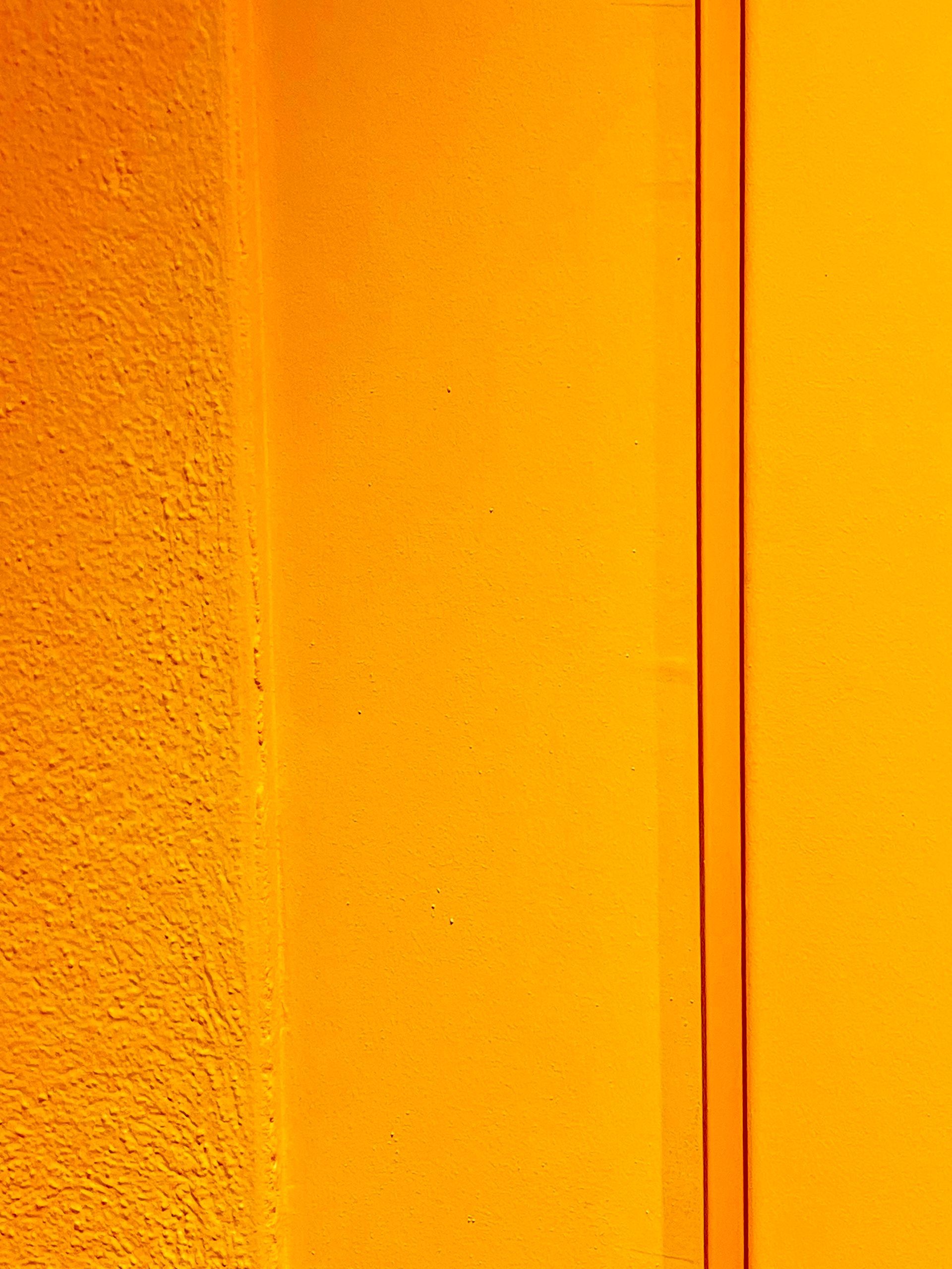 Eine leuchtend gelb-orange Wand mit einer strukturierten Oberfläche auf der linken Seite und einem glatten Abschnitt mit vertikaler Zierleiste.