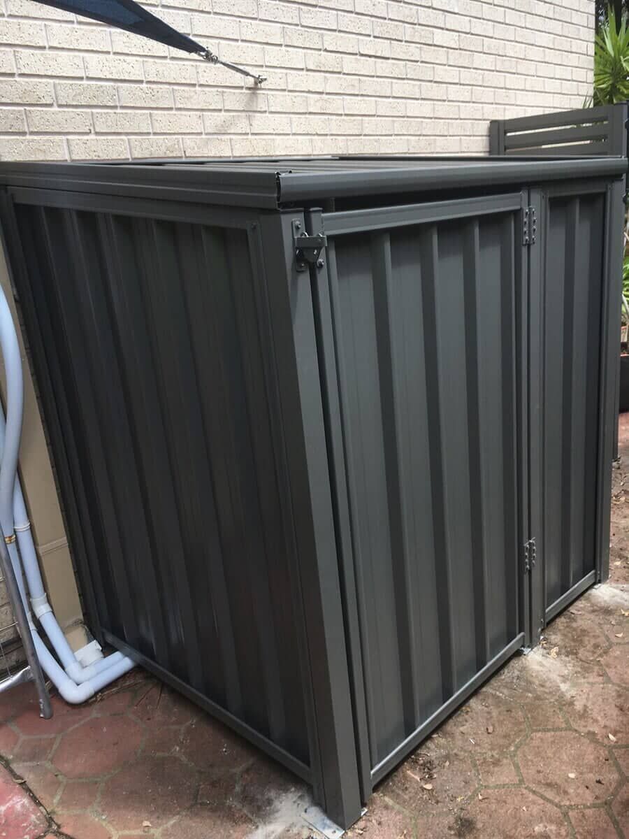 A Black Metal Shed is Sitting on the side of a Brick Building — Fencing in Port Stephens, NSW