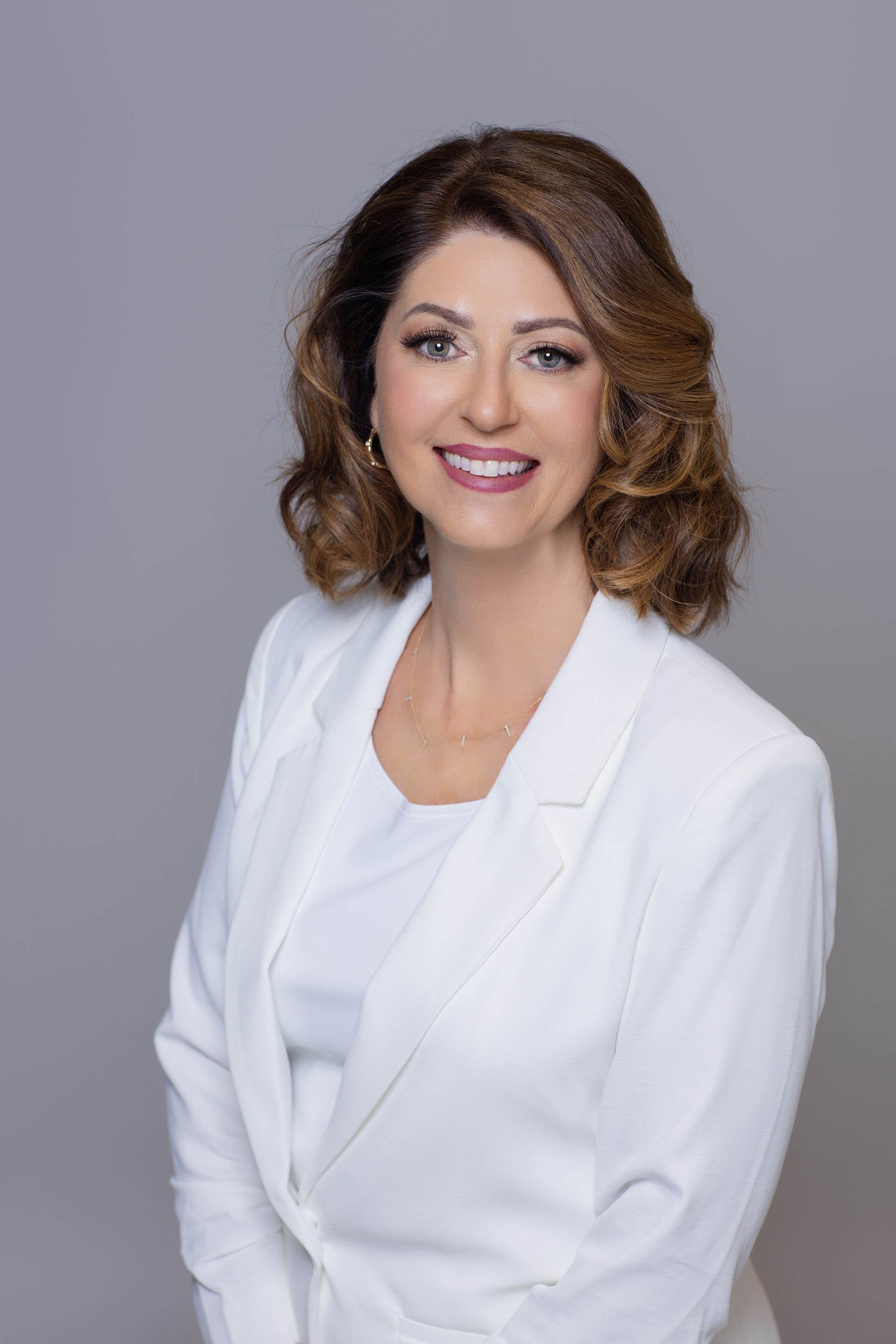 A woman in a white jacket and white shirt is smiling for the camera.