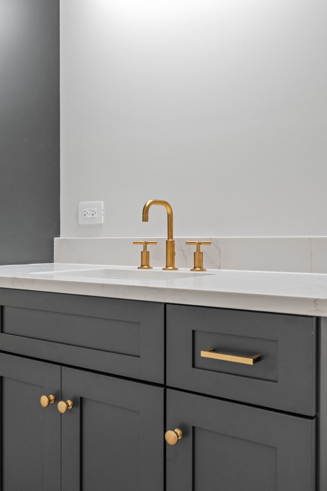 A bathroom sink with gray cabinets and a gold faucet.