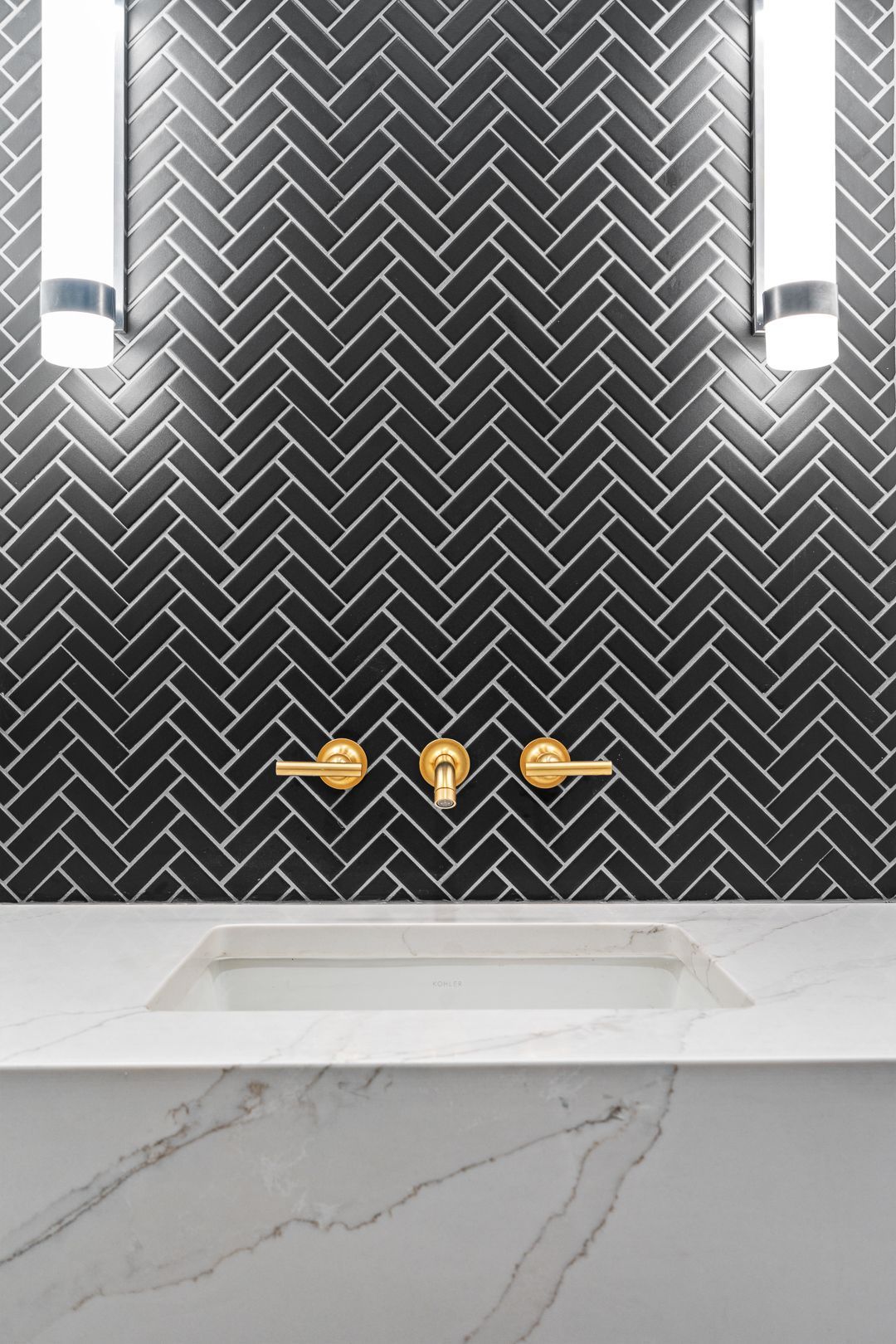 A bathroom with black herringbone tiles and a sink.