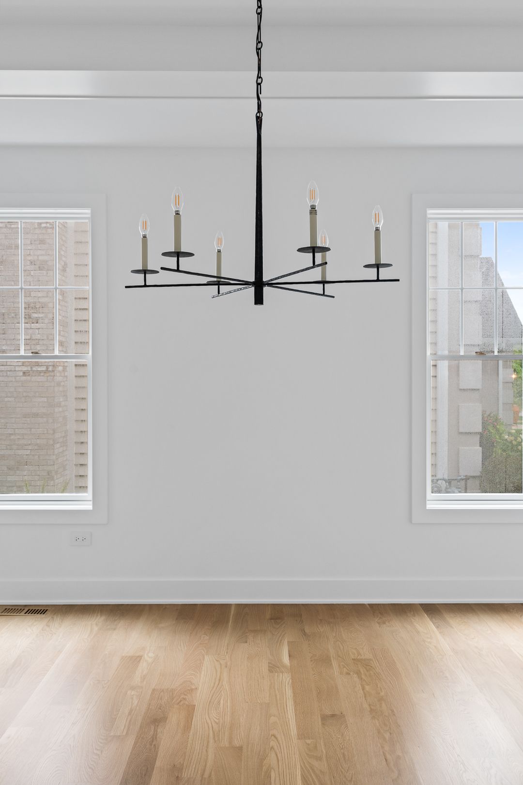 An empty room with hardwood floors and a chandelier hanging from the ceiling.