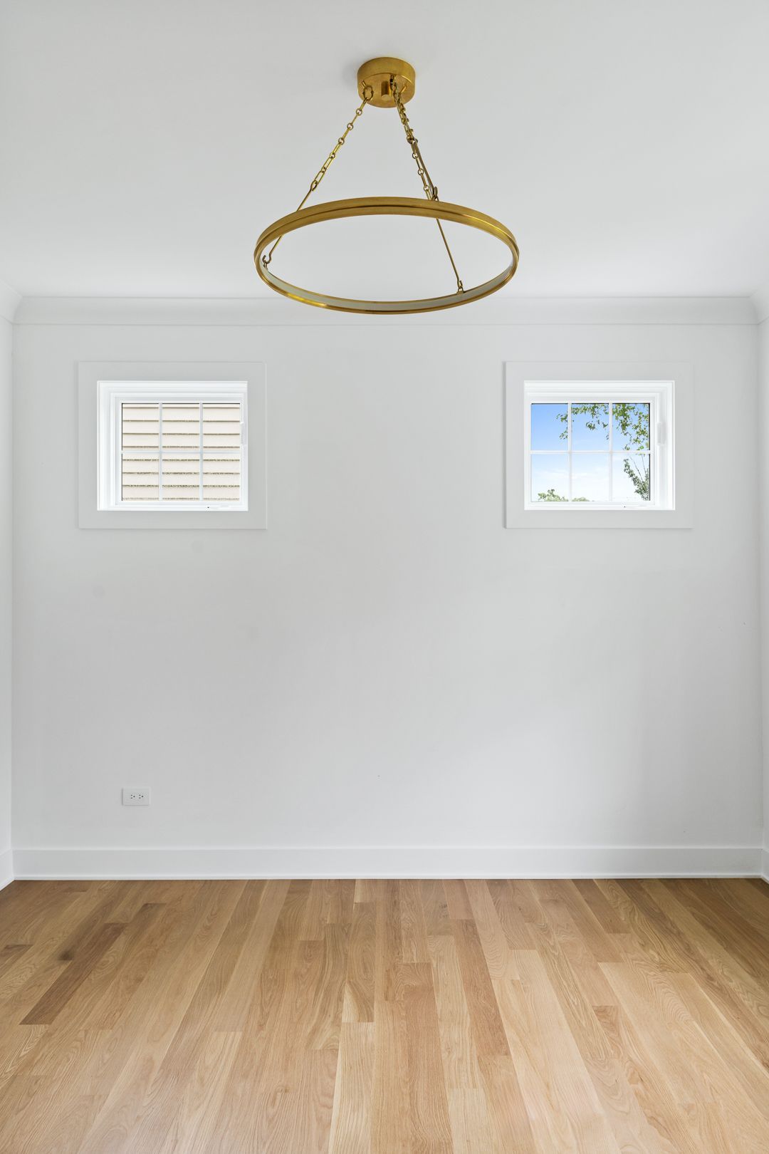 An empty room with two windows and a chandelier hanging from the ceiling.