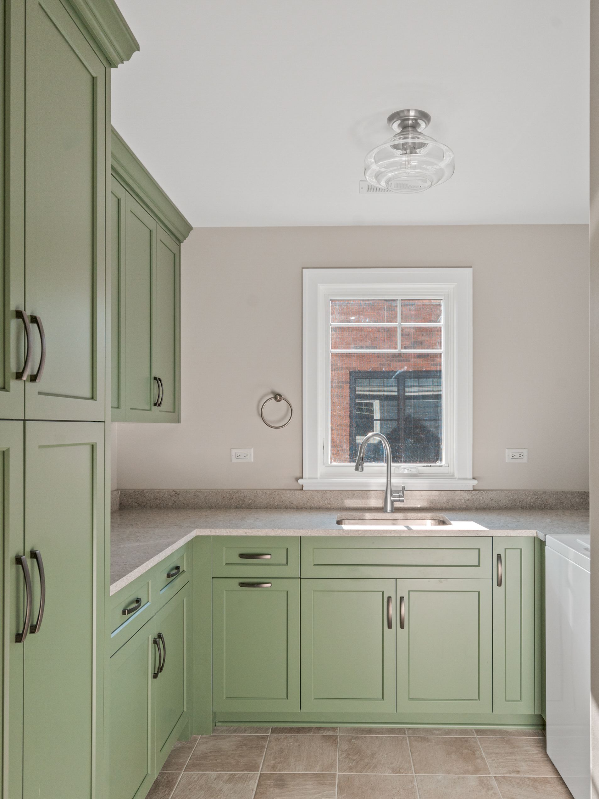 A kitchen with green cabinets , a sink , and a window.