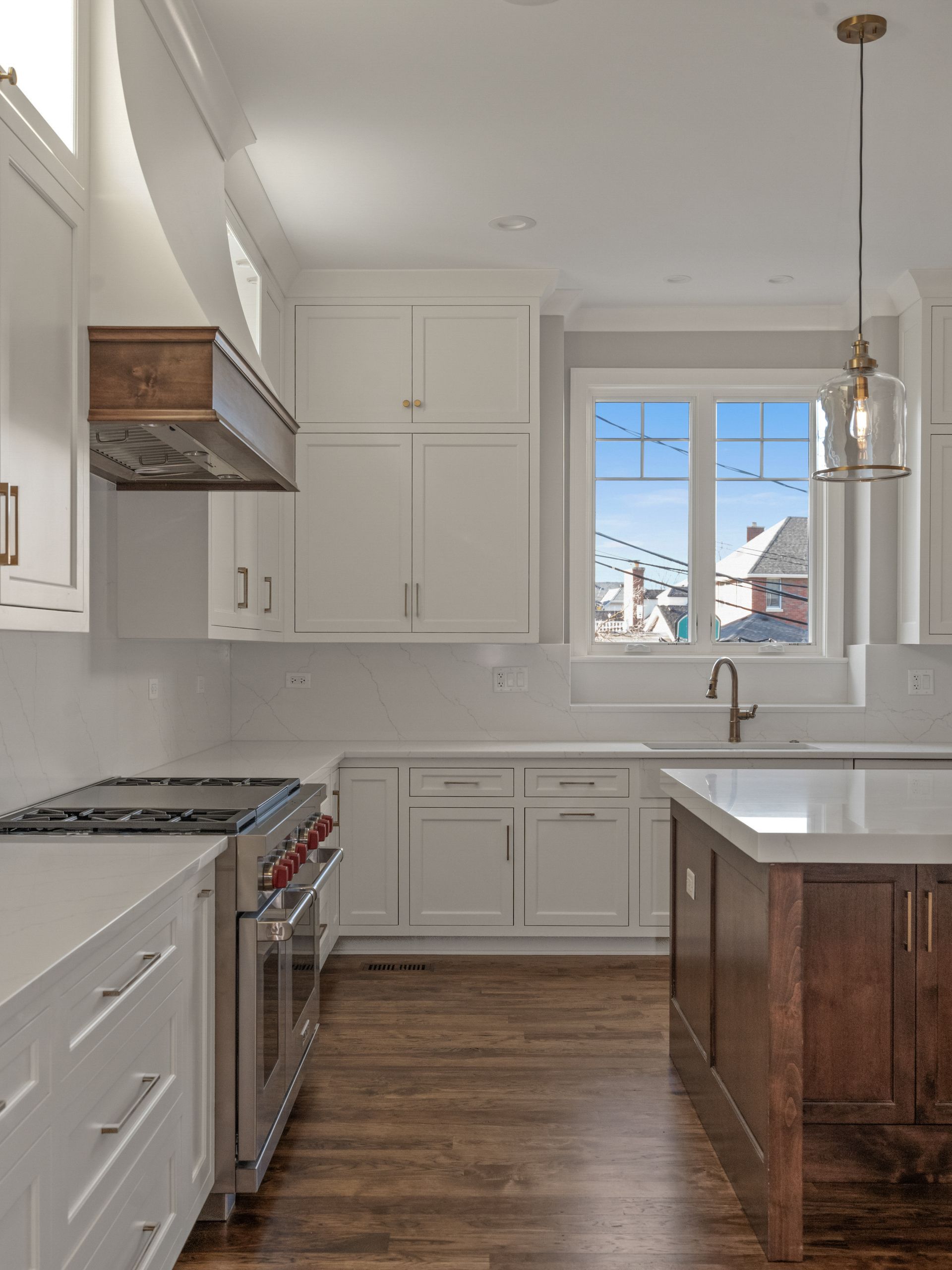 A kitchen with white cabinets , a stove , a sink , and a window.