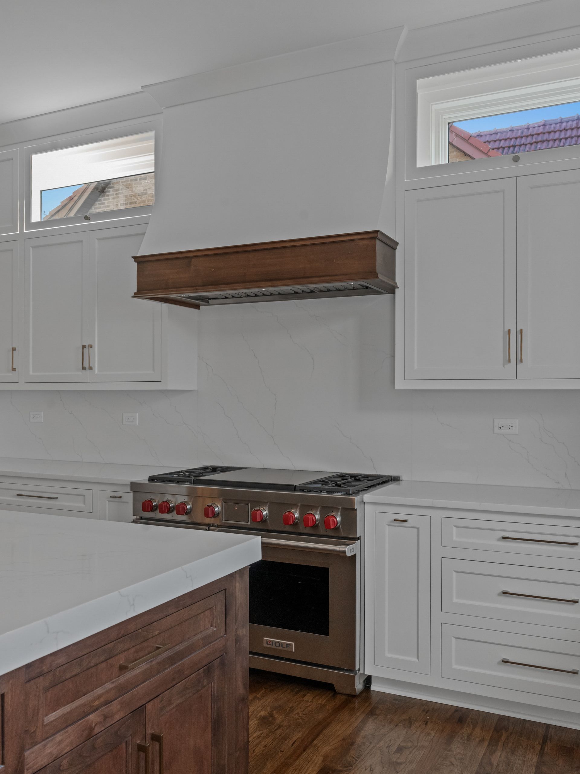 A kitchen with white cabinets , a stove , and a window.