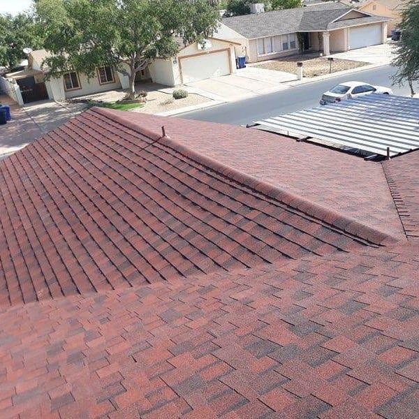 Red asphalt shingle roof on a house, with a street and other houses in the background.