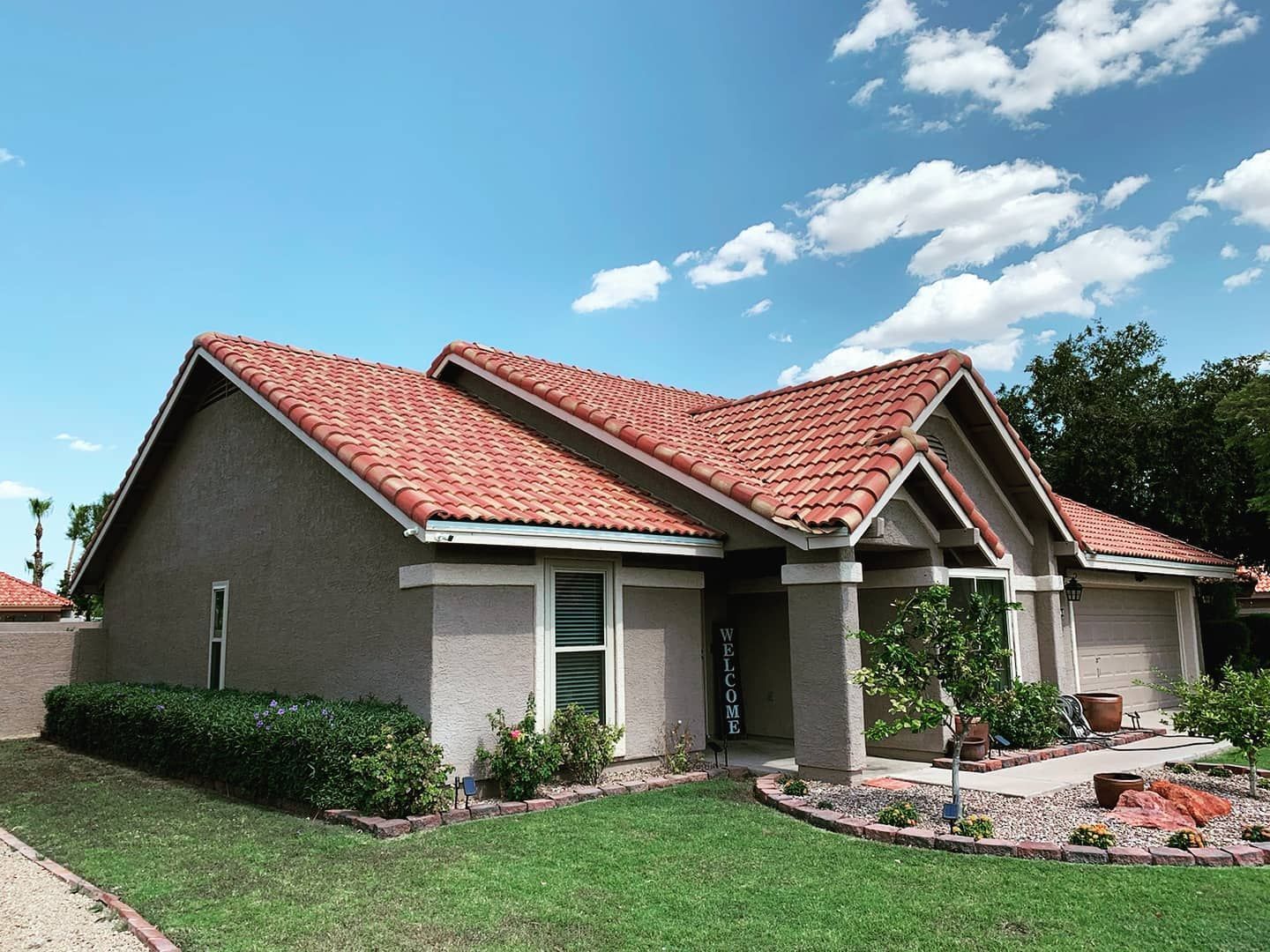 House with red tile roof and stucco walls, green lawn, blue sky with clouds.