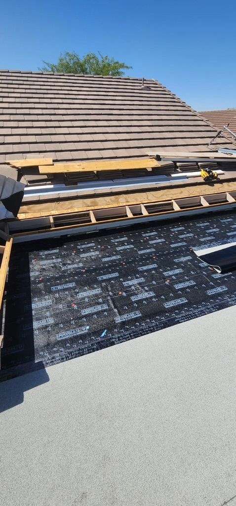 Roof partially stripped, revealing layers. Brown tiles, exposed wooden beams, and black underlayment visible. Blue sky.