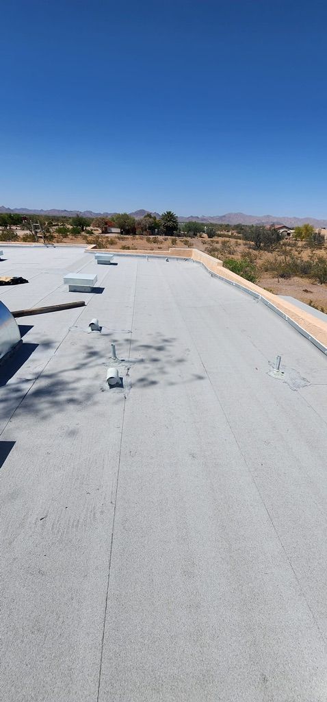 View of a flat, gray roof with vents and a desert landscape under a clear blue sky.
