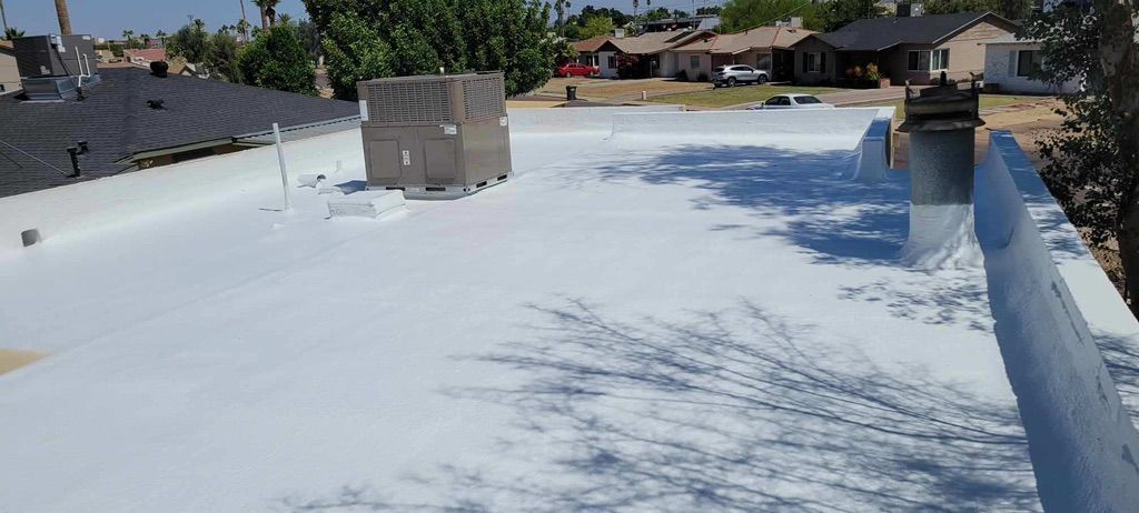 A white roof with shadows from trees. Buildings and palm trees are in the background.