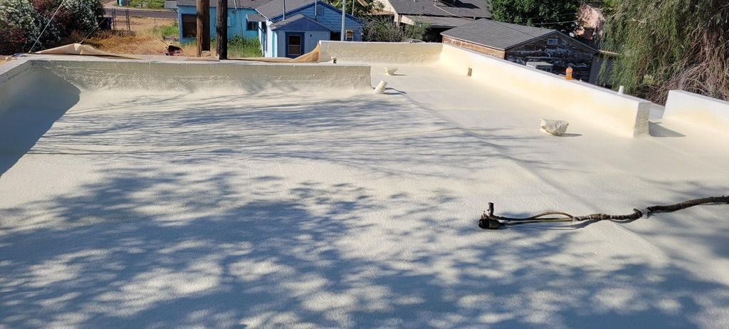 A flat, light-colored rooftop with shadows.  In the background, a residential neighborhood with blue houses and trees.
