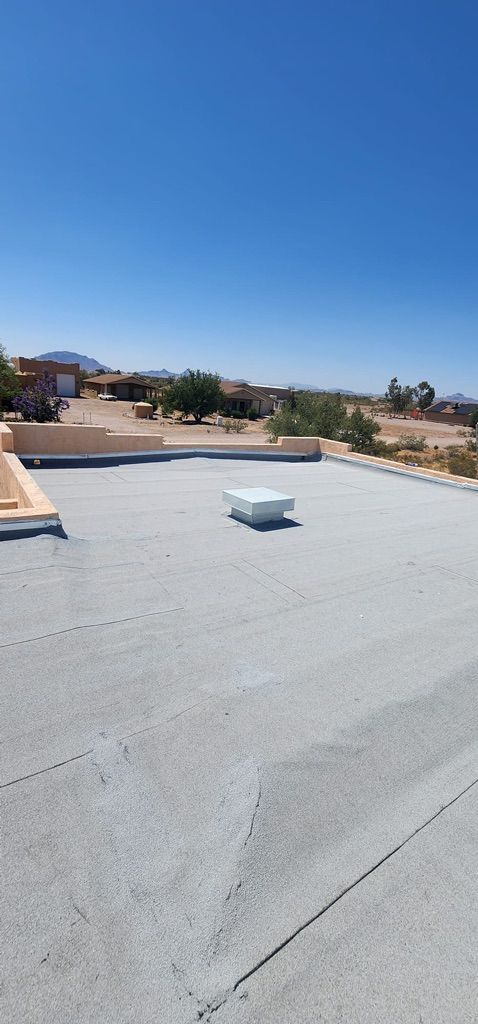 A flat roof with a skylight under a bright blue sky overlooking a desert landscape.