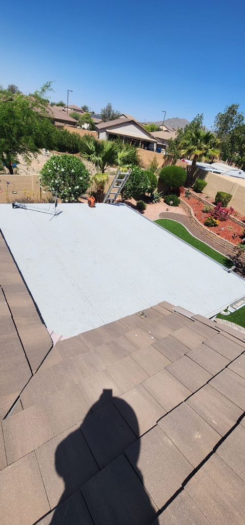A rectangular pool covered with a white tarp, surrounded by greenery and homes, viewed from a roof on a sunny day.