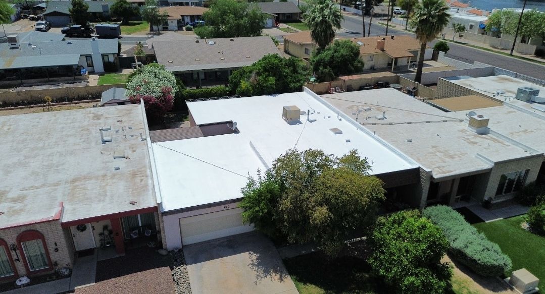 Aerial view of residential homes with white flat roofs and a street lined with trees.