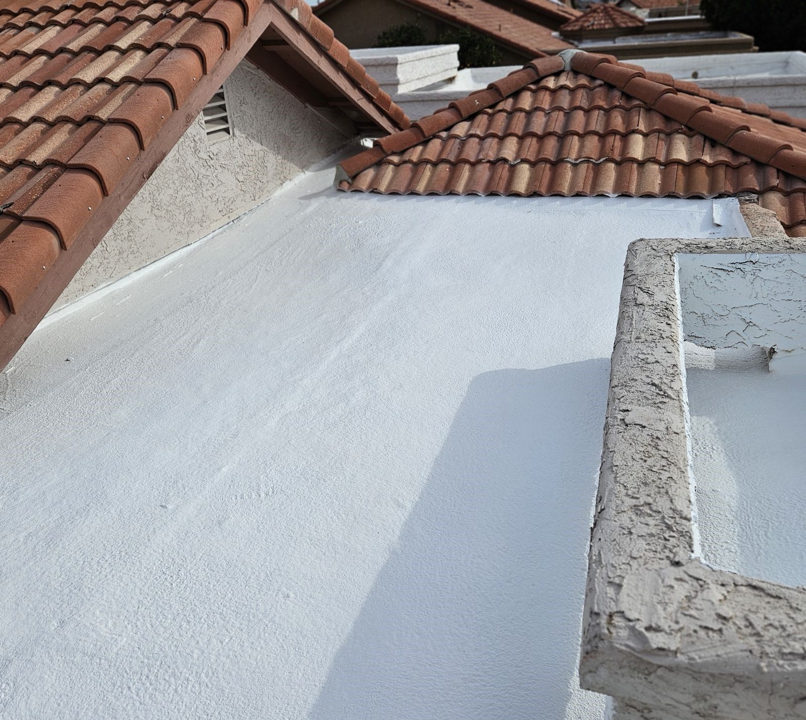 White stucco roof with terracotta tile roof section in background.