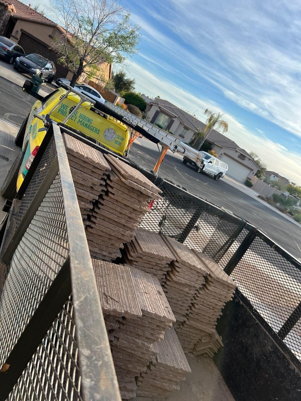 A truck bed full of stacked, brown tiles on a residential street. A company truck is nearby.