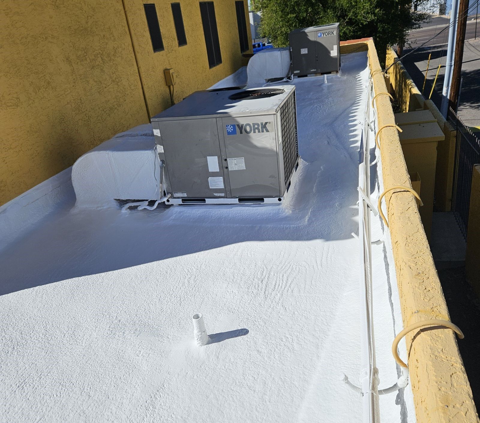 White-coated flat rooftop with HVAC units, yellow building, and a railing on the side.