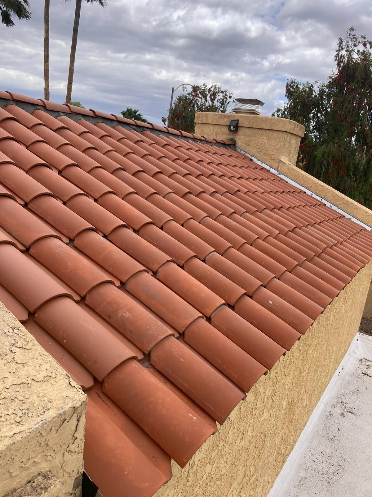 Orange tile roof on a stucco building with a chimney and cloudy sky in the background.