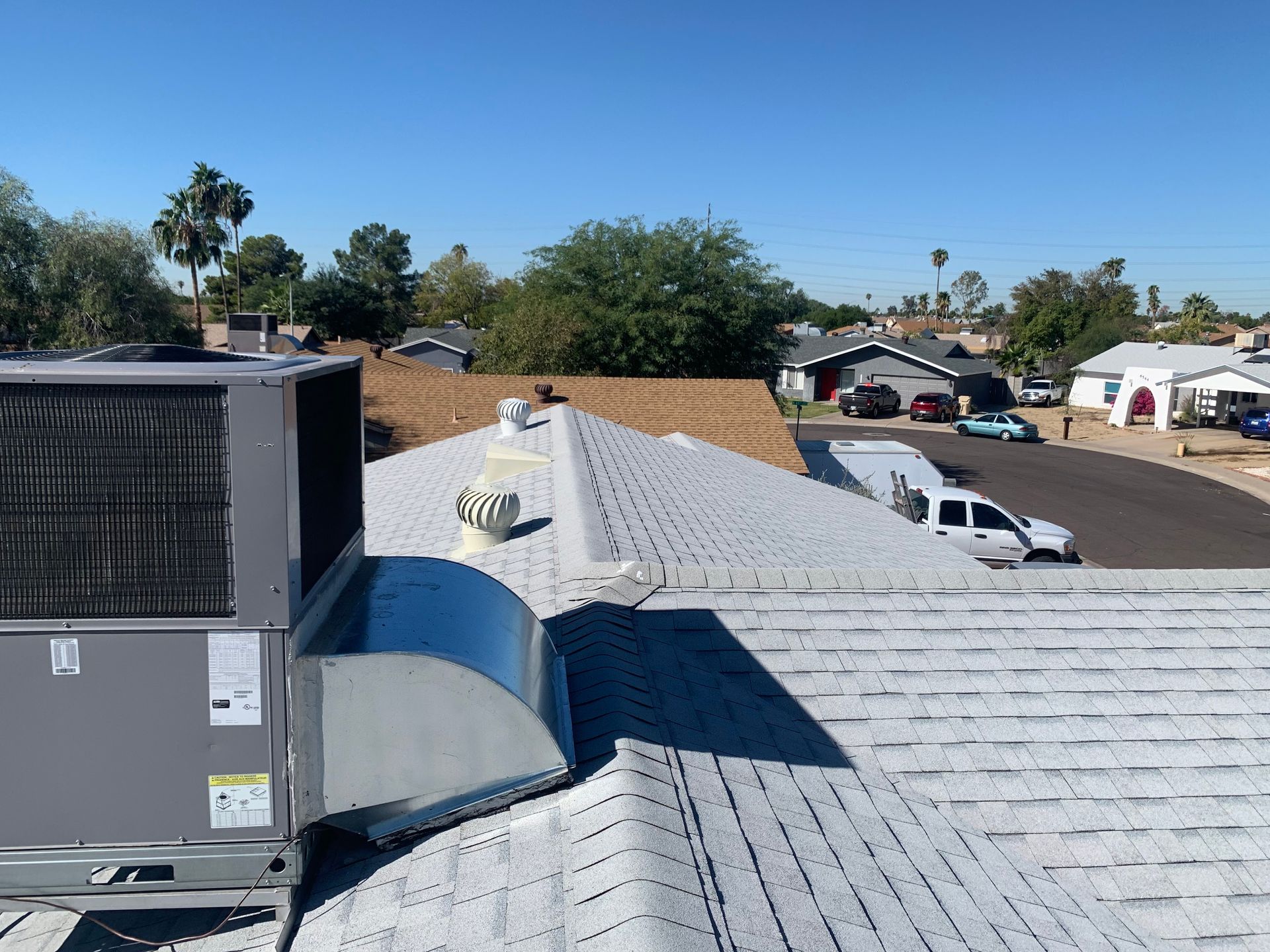 Rooftop with HVAC unit, vents, and a white pickup truck. Clear blue sky, suburban setting.