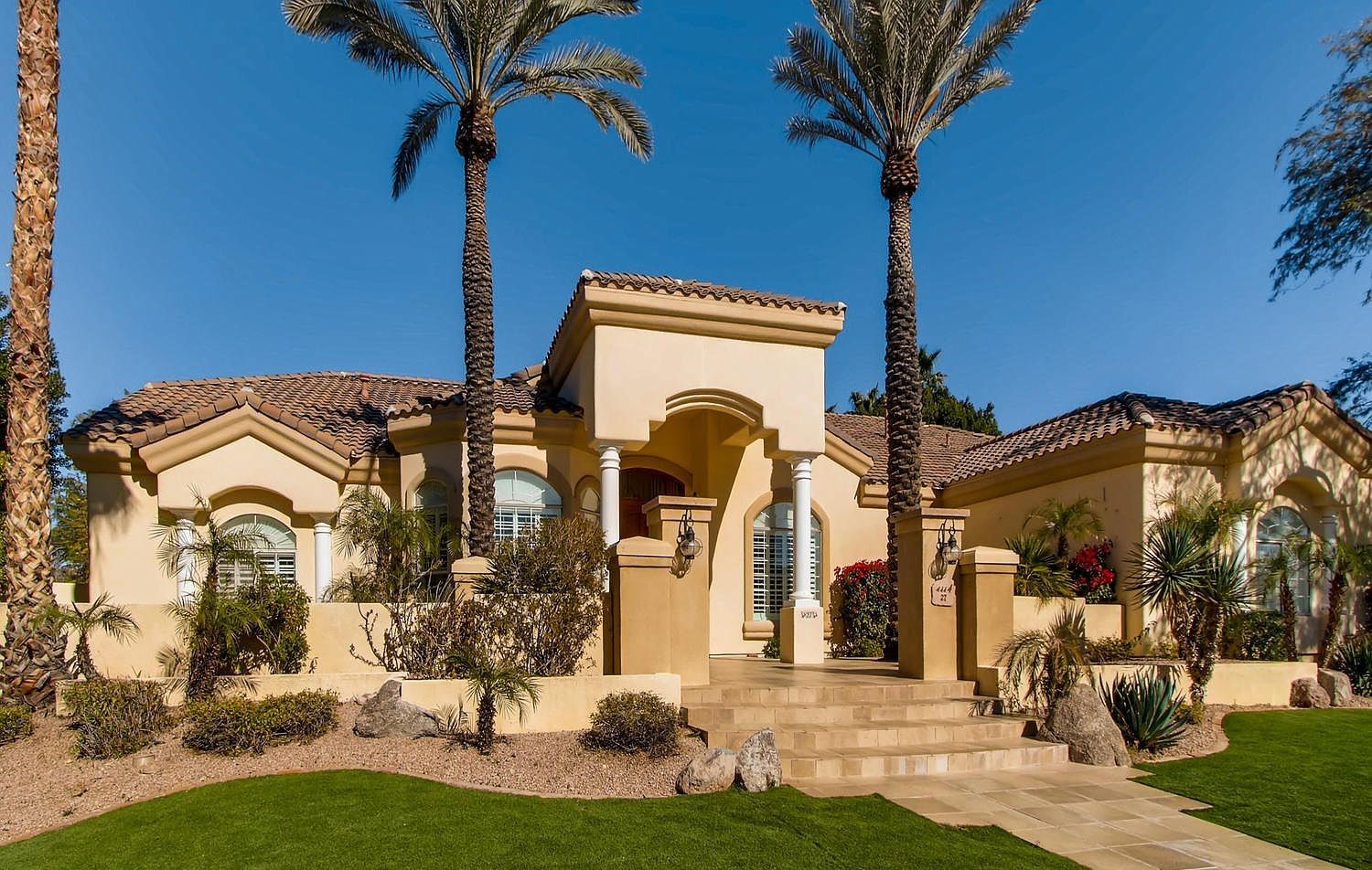 Beige stucco home with palm trees and a blue sky.