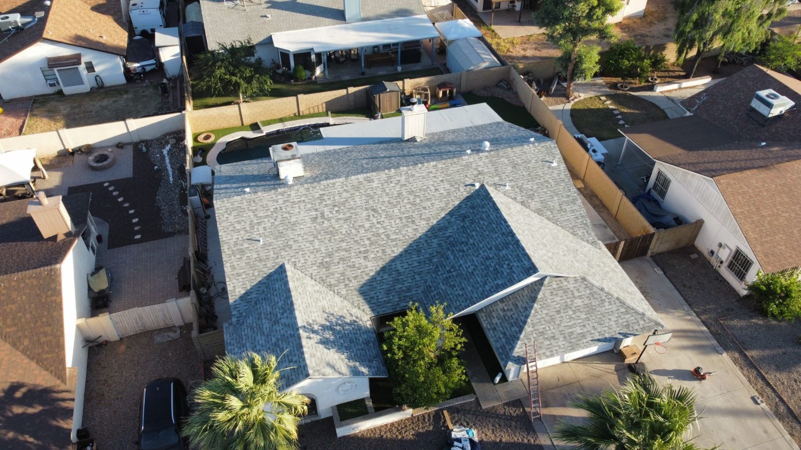 Aerial view of a suburban house with a gray shingle roof, surrounded by other houses and trees.
