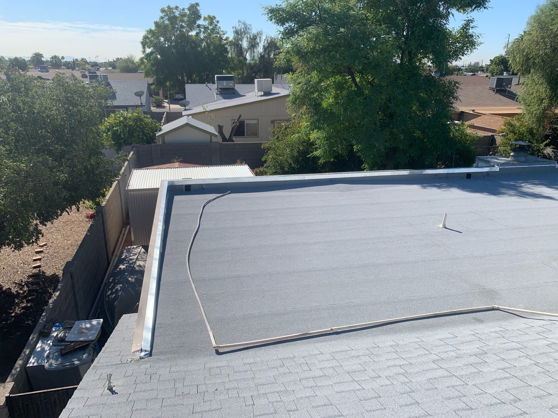 A flat, gray roof with metal edging, overlooking a suburban neighborhood on a sunny day.