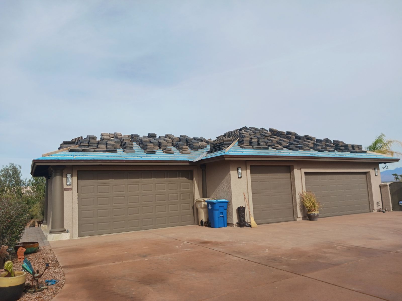 Garage with roof under construction, stacks of dark tiles on blue underlayment.