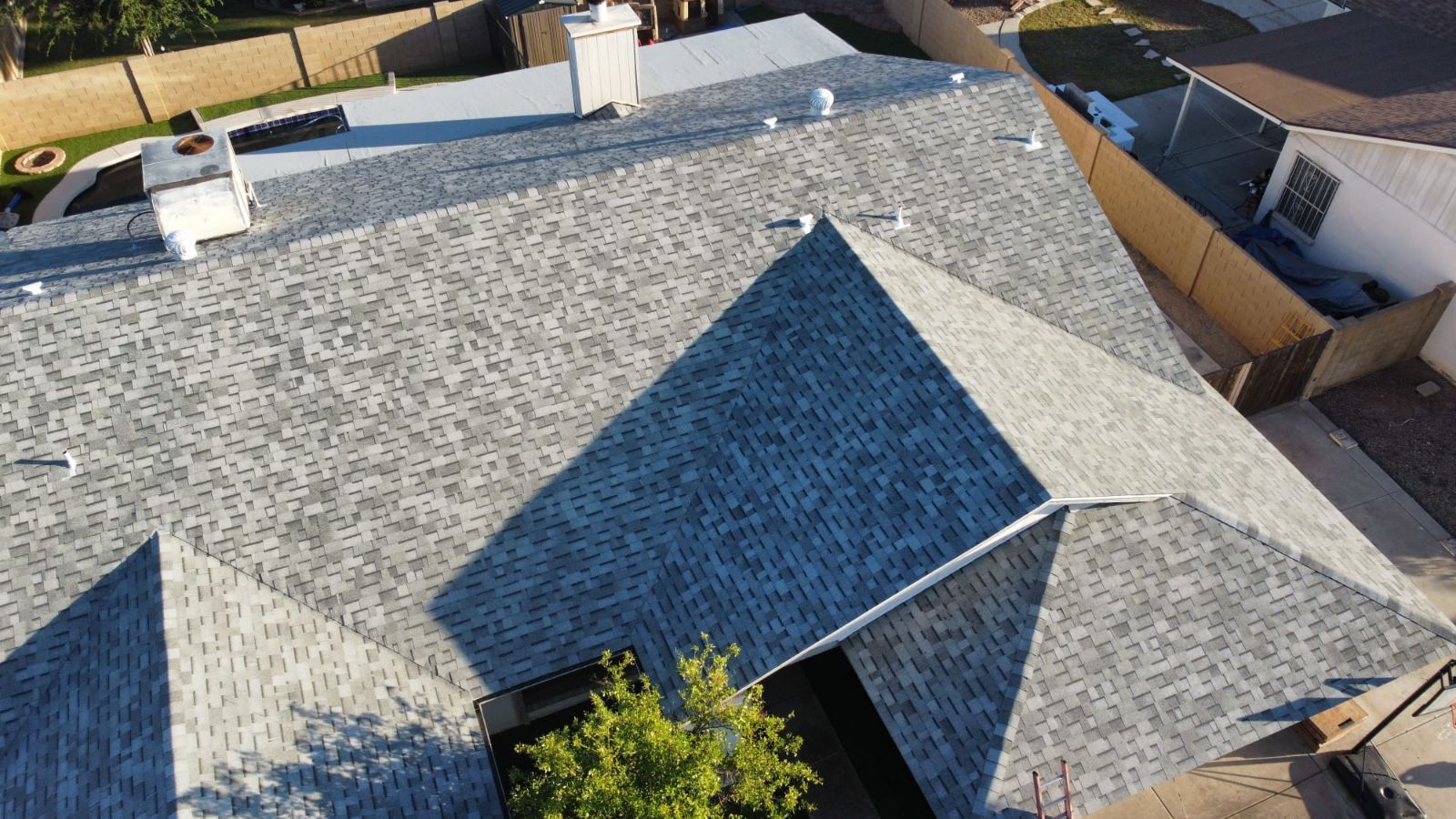 Aerial view of a gray shingled roof with a chimney and sunlight creating shadows.