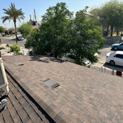 Brown shingled roof with a view of a street, cars, and trees on a sunny day.