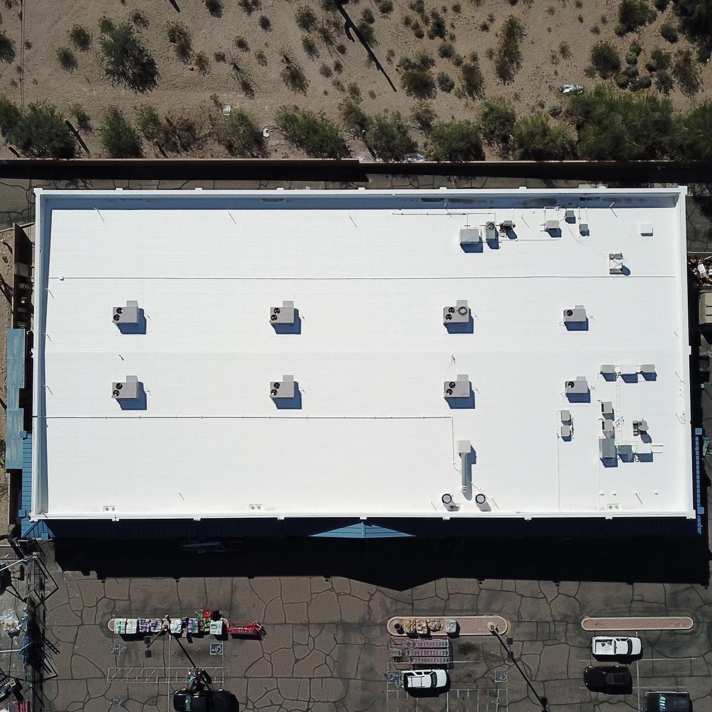 Overhead view of a large white commercial building with vents on the roof, surrounded by parking and desert vegetation.