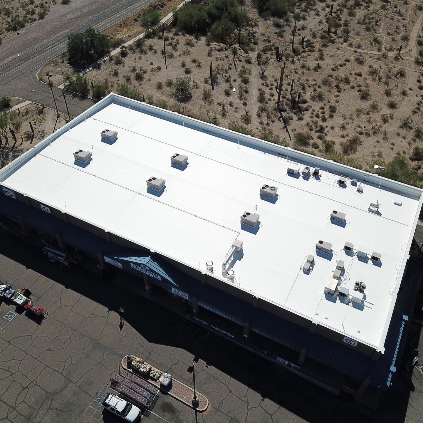 Aerial view of a white-roofed commercial building in a desert setting; several rooftop HVAC units are visible.