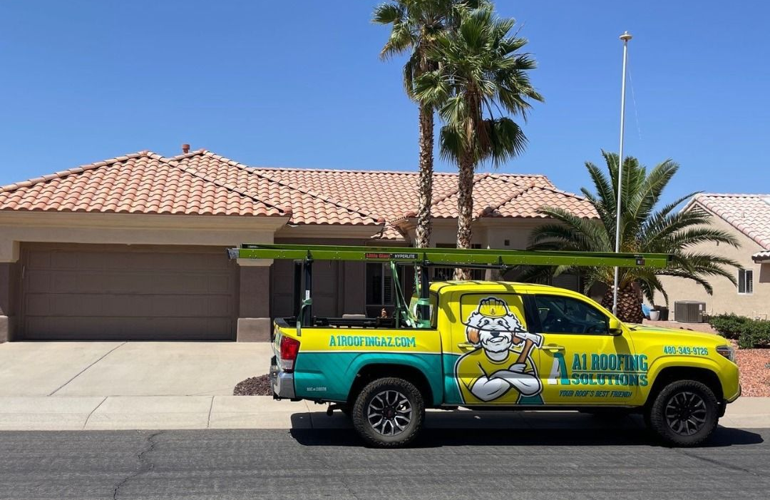 Yellow and teal work truck parked in front of a house, carrying equipment on the roof.