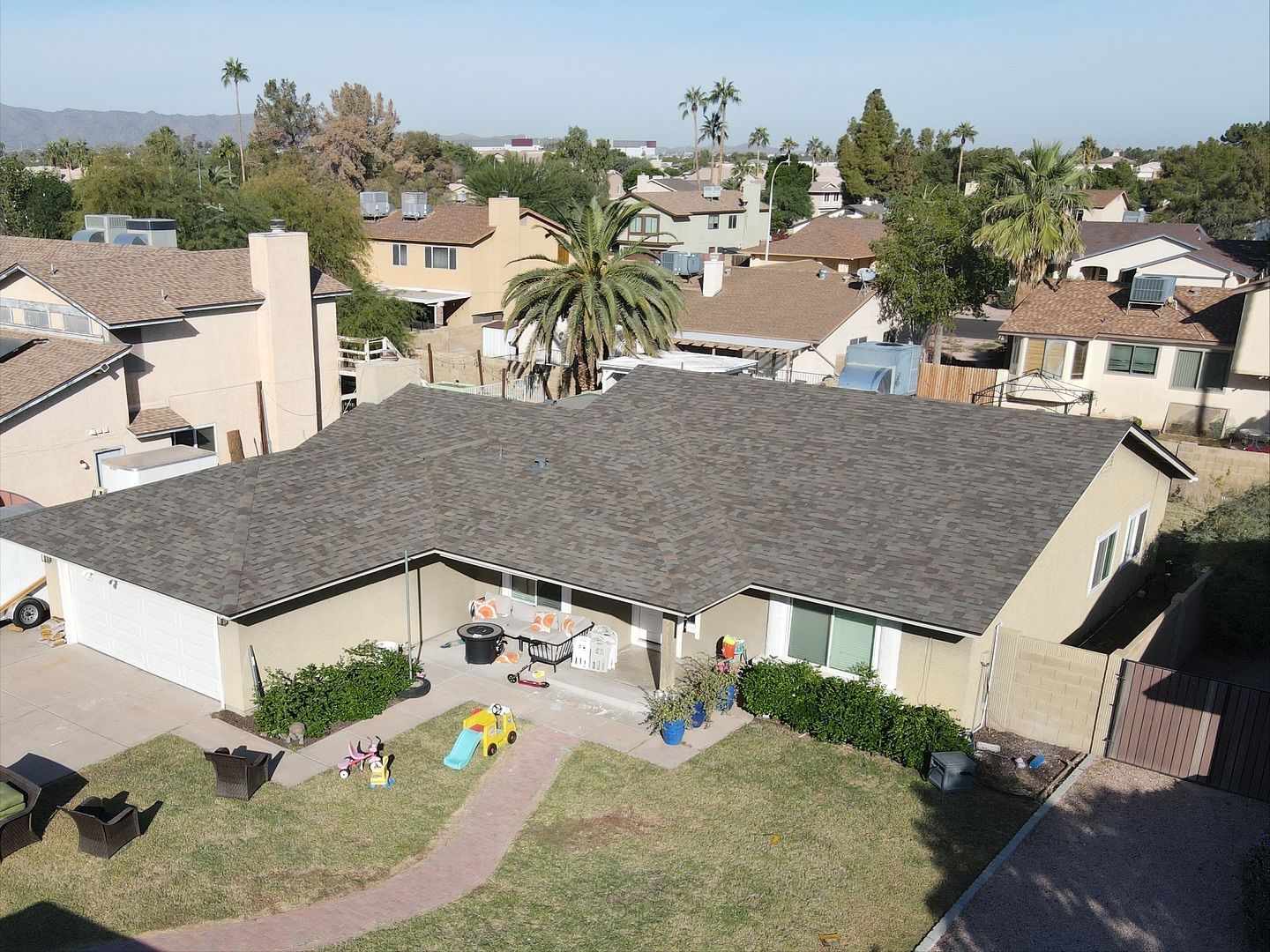 Aerial view of a beige house with a dark gray roof in a suburban neighborhood.