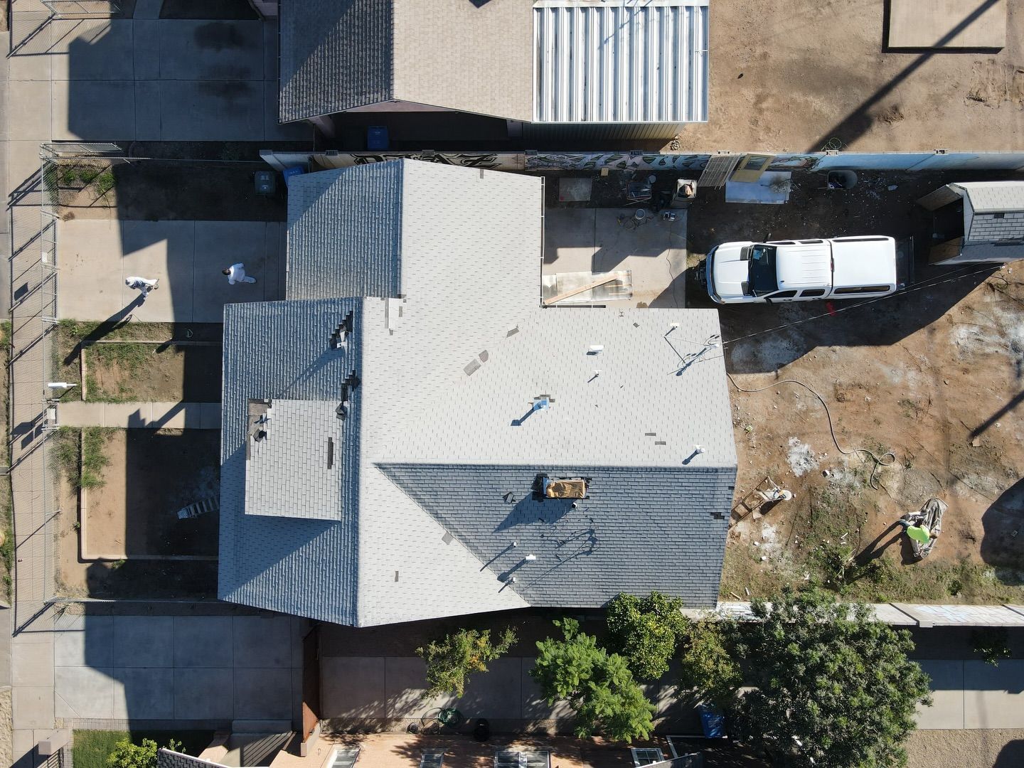 Aerial view of a house with a gray roof, a white van parked nearby, and a brown yard.