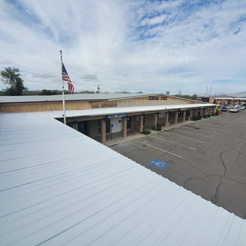 Shopping center with covered walkways, parking lot, American flag, and overcast sky.