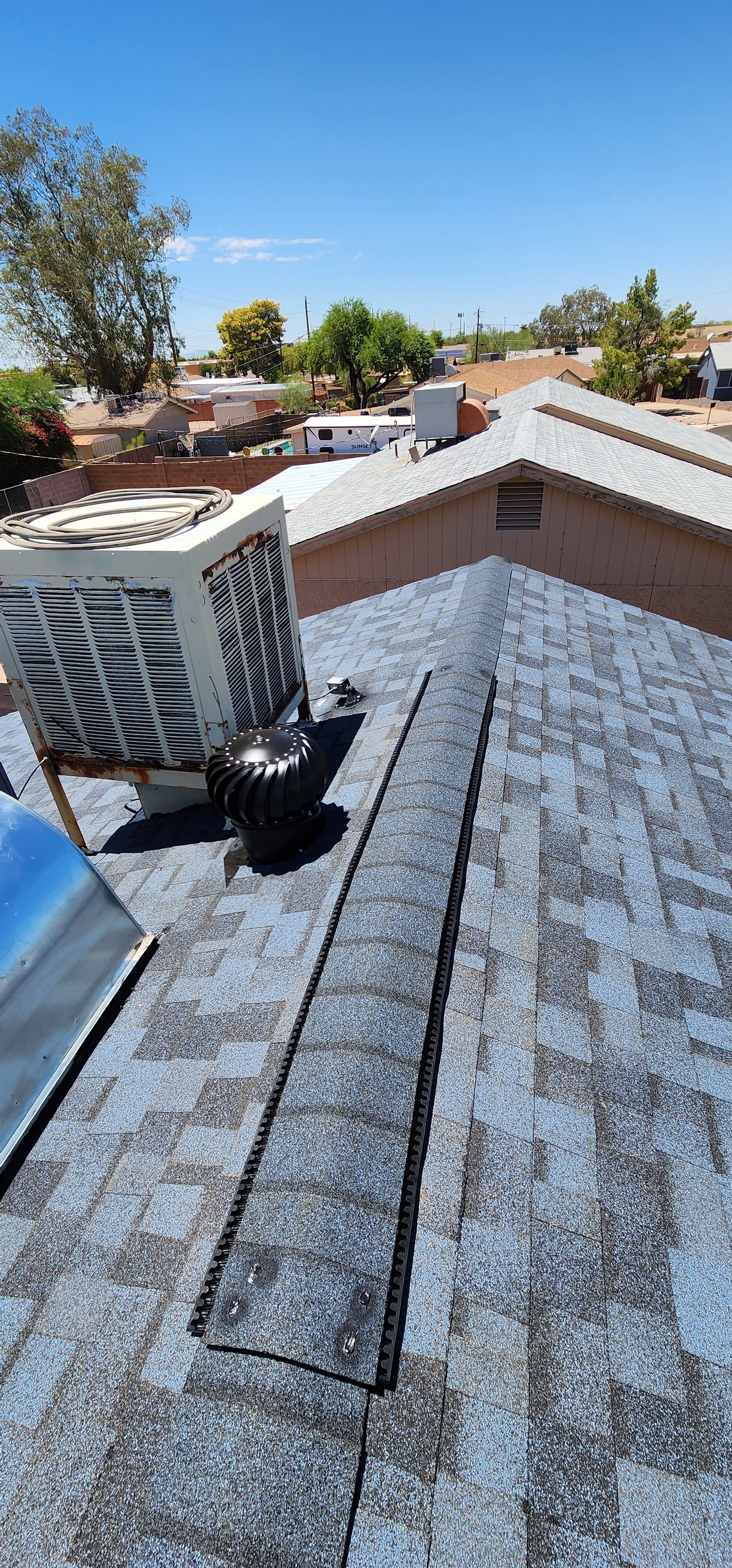 View from a roof, featuring a roof vent, air conditioner, and cityscape under a blue sky.
