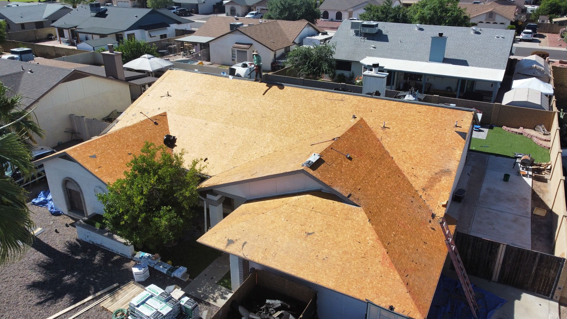 House roof being repaired; new shingles installed. Brown shingles, blue tarp, residential neighborhood.