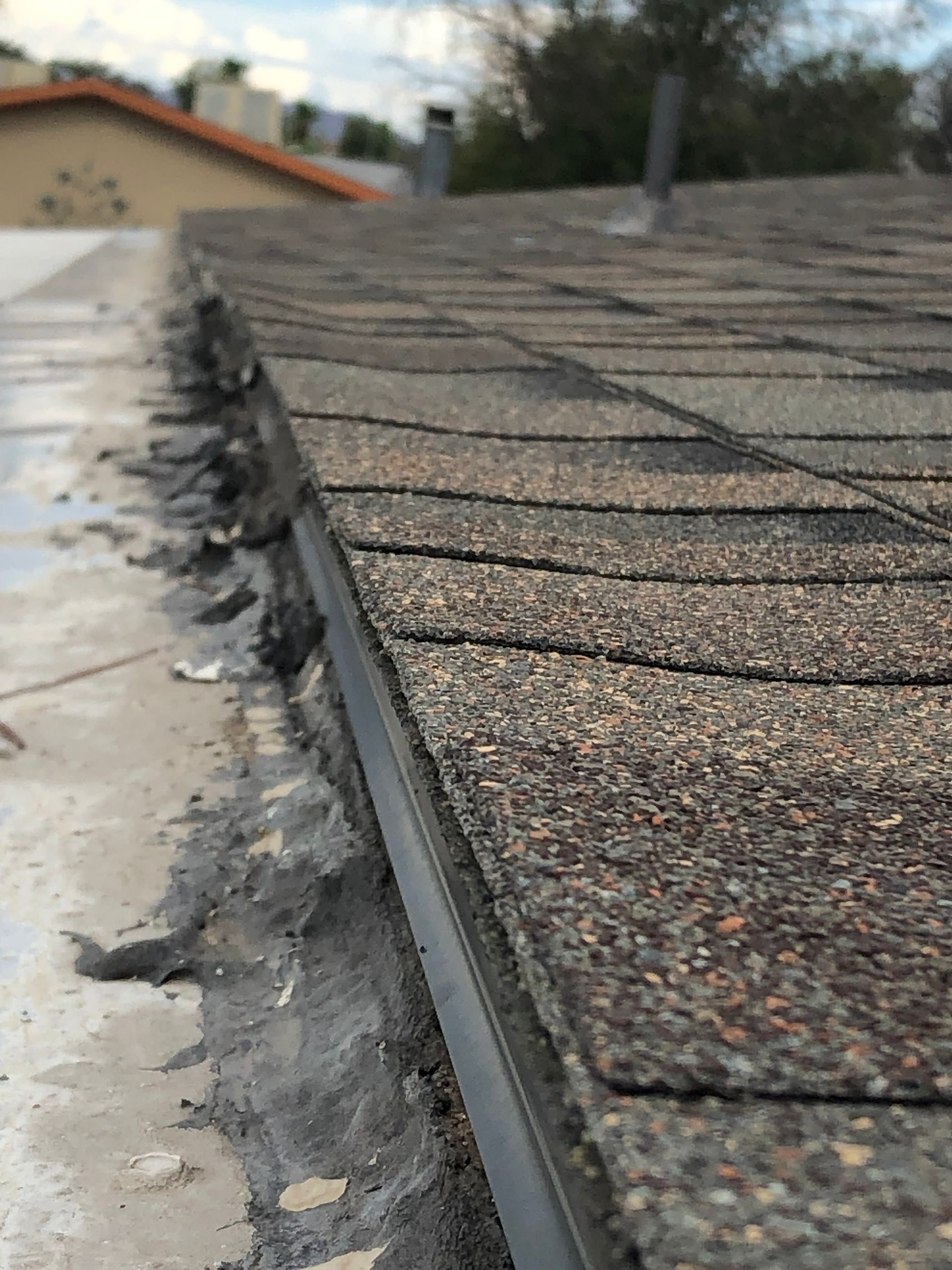 Close-up of a house roof edge with asphalt shingles and a flat roof section.